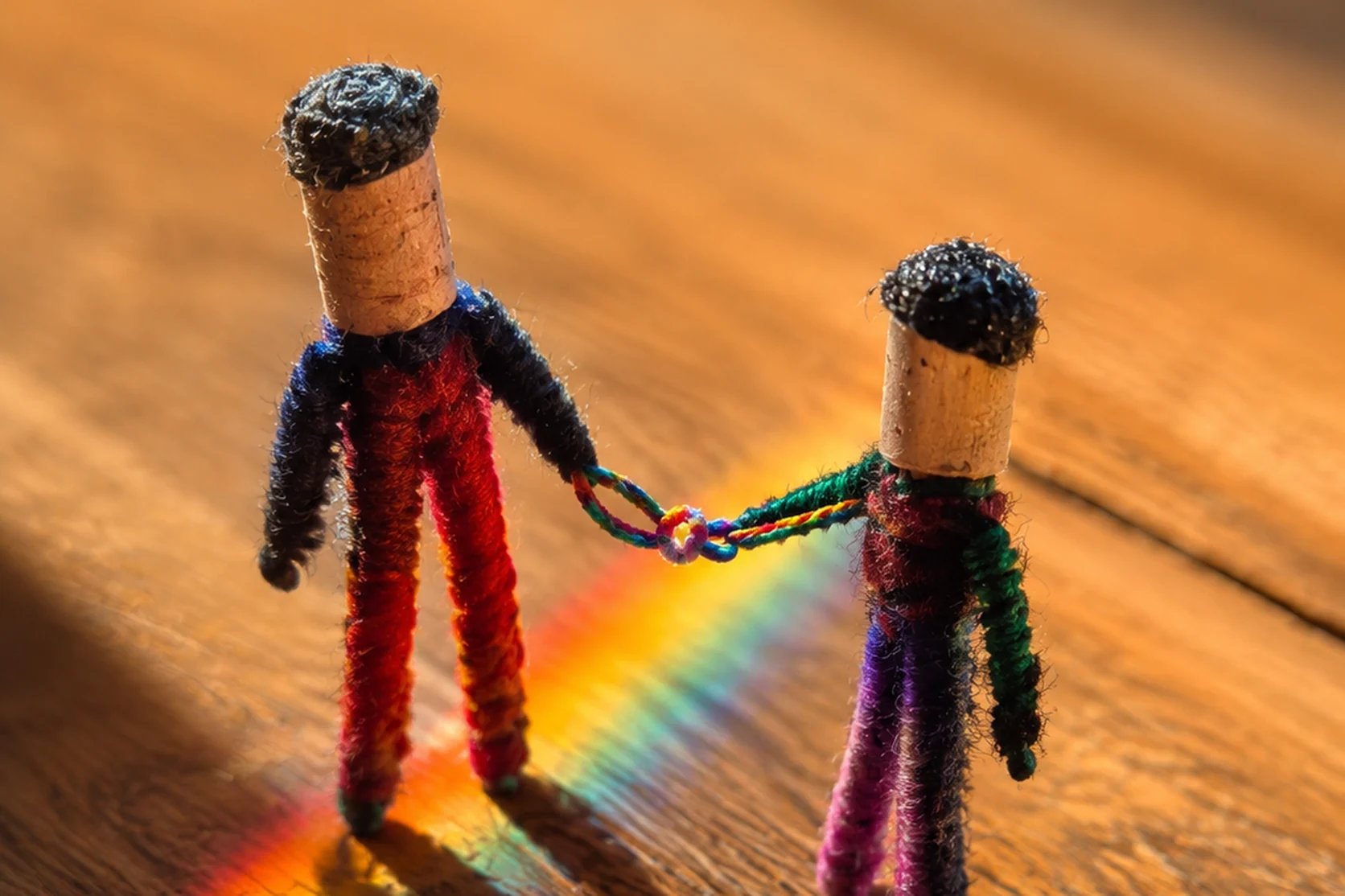 Deux figurines reliées par la main, traversées par un arc-en-ciel
